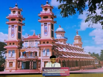 A representative of Cao Dai with an image of the main Cao Dai temple in Vietnam behind him